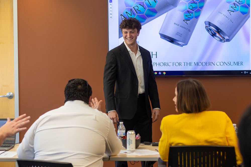 Logan Milano presenting in front of a screen with 'AMRYTH' branding, seated people listening.